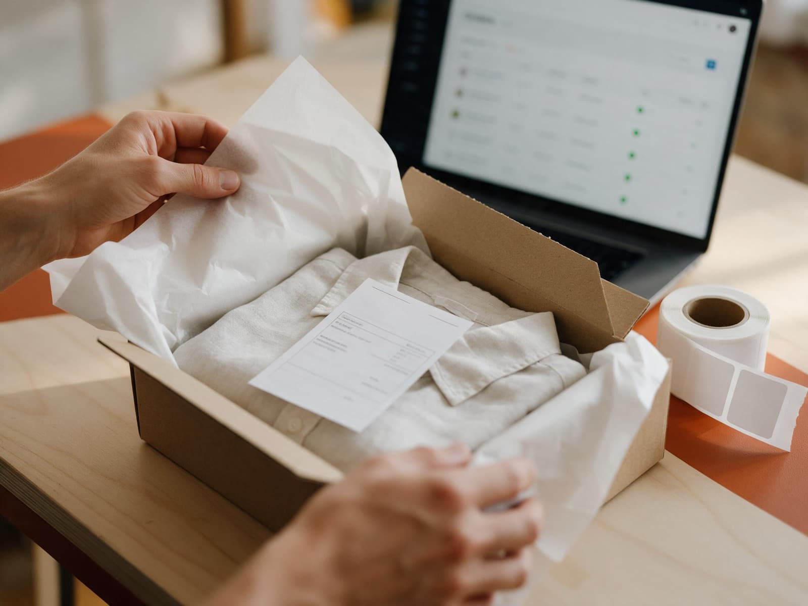 Order being packed into a kraft shipping box with an orders dashboard in the background